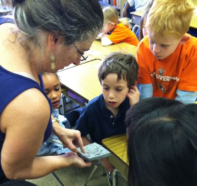 A teacher showing a group of young children a textured material in a classroom setting.