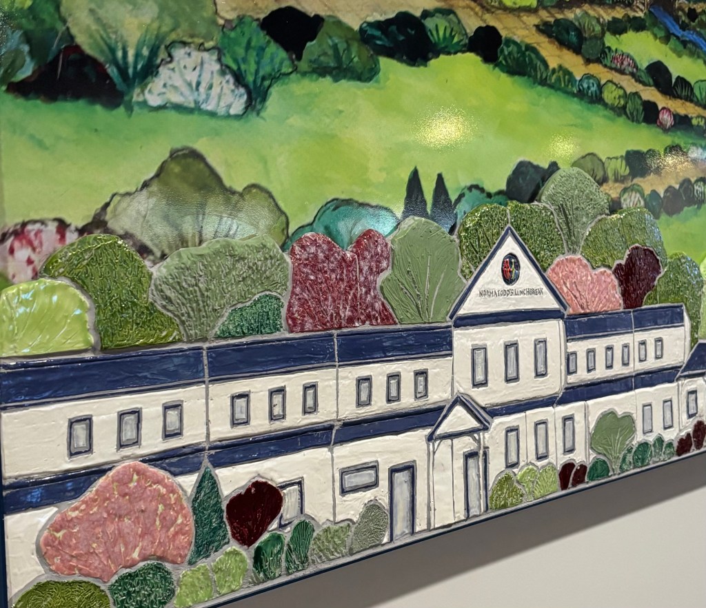 A decorative ceramic artwork depicting a building surrounded by colorful vegetation.