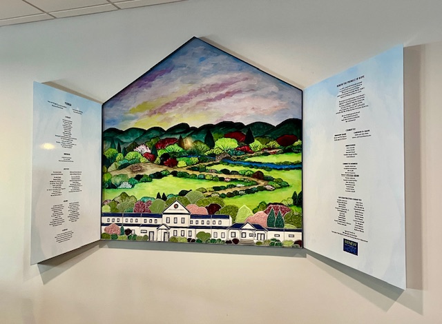 A large artwork depicting a colorful landscape with rolling hills, trees, and a building in the foreground, framed by two white panels featuring text.